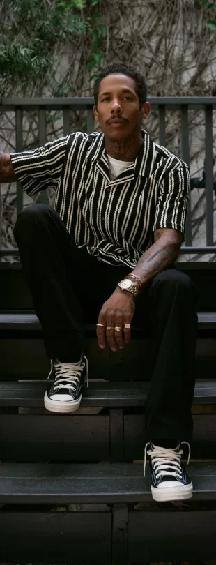 Man in striped shirt sitting on stairs with hands clasped