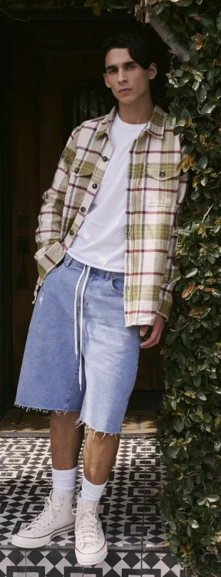 Man in plaid shirt and denim shorts standing by a door